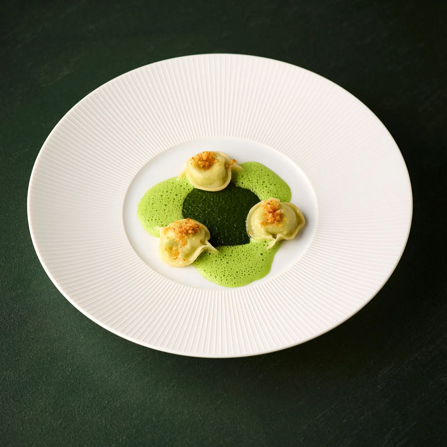 Sellerie mit Perigord Trüffel und Haselnuss in einer grünen Schaumsoße auf einem weißen Teller angerichtet. Teil des Green Forest 8-Gänge-Menüs im Ammolite.