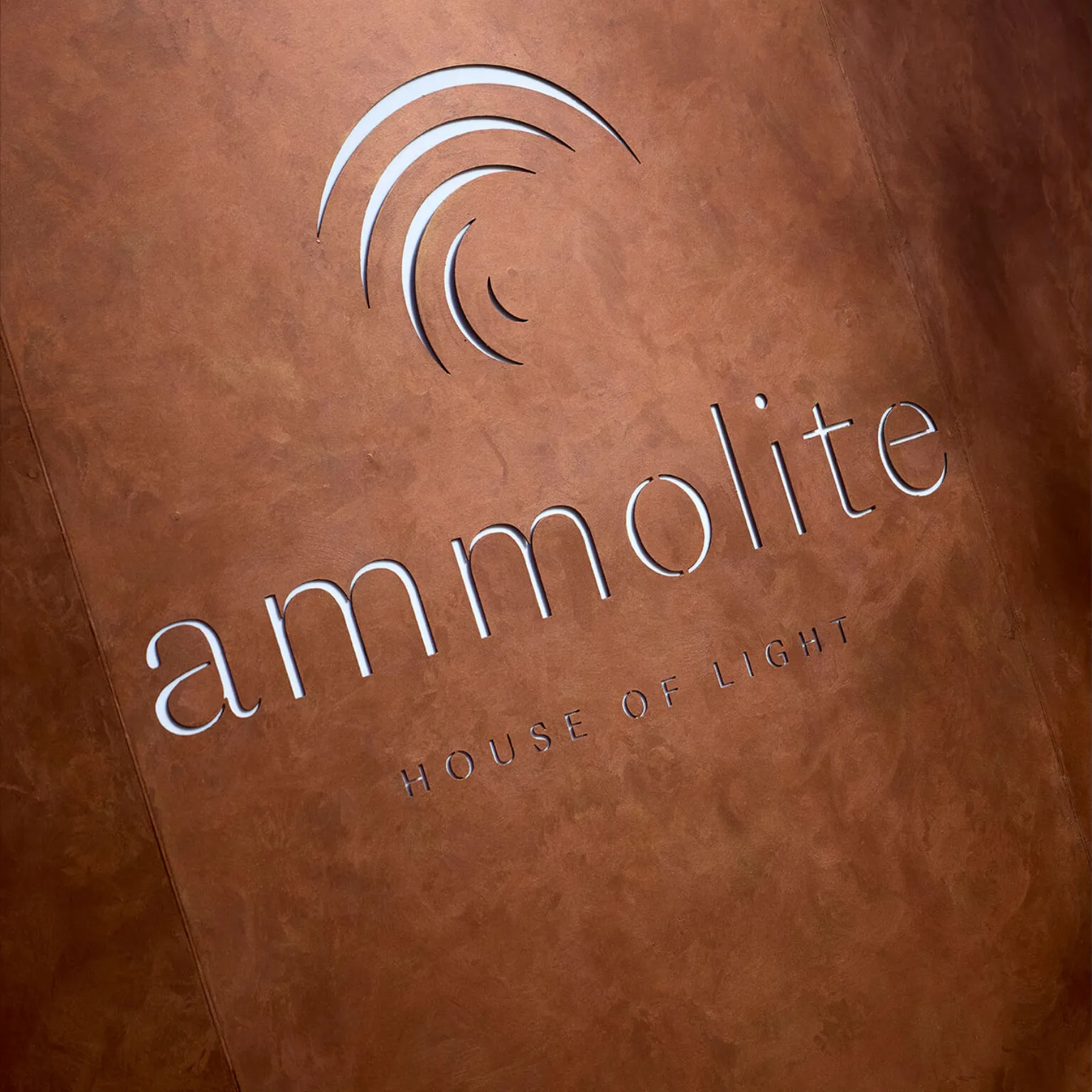 Der Schriftzug Ammolite – House of Light auf einer kupferfarbenen Wand.